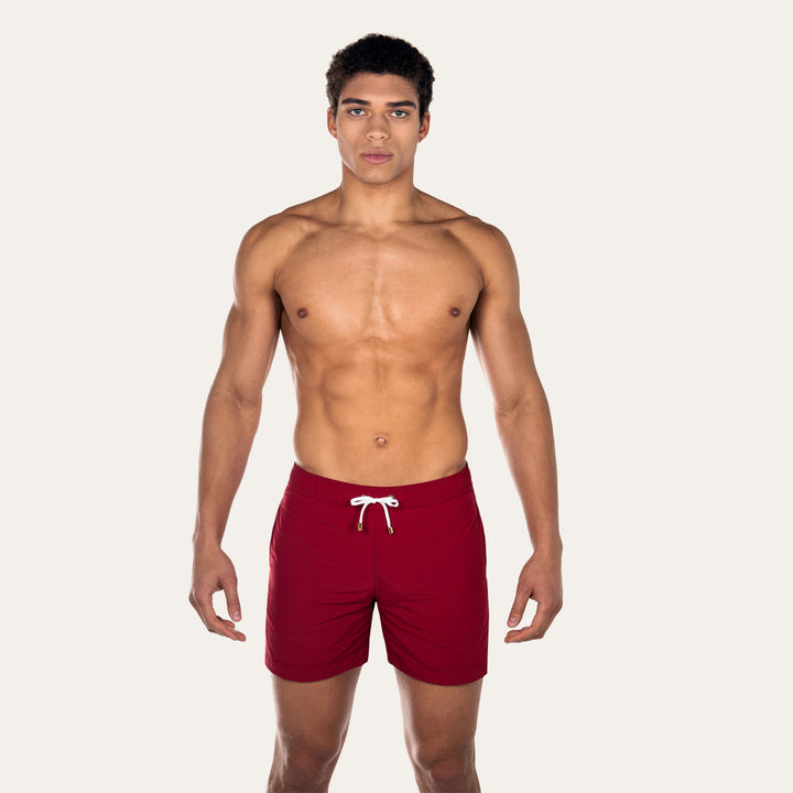 Model is wearing burgundy Easton tailored swim shorts by Prince & Bond
