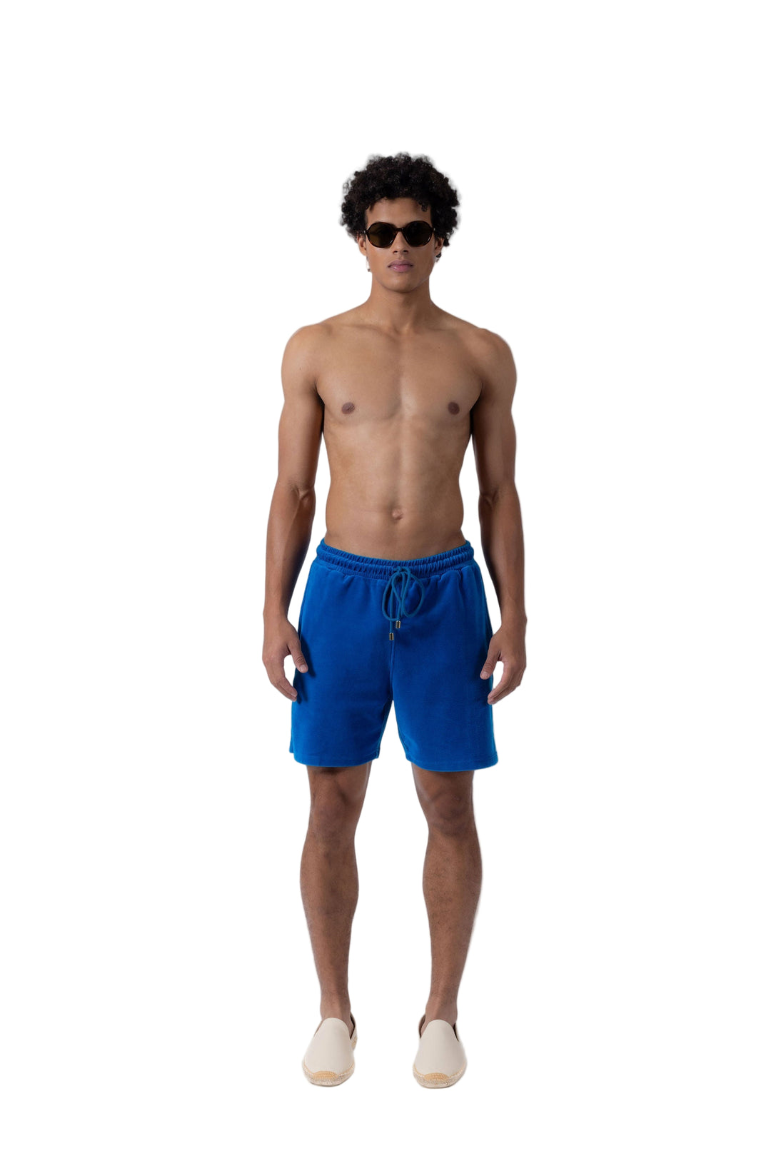 Model wearing Prince & Bond Riviera Terry Cloth shorts in Mykonos Blue styled with sunglasses on a neutral background 