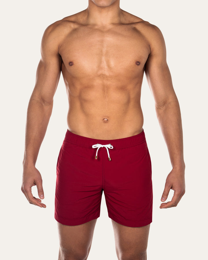 Model is wearing burgundy Easton tailored swim shorts by Prince & Bond
 